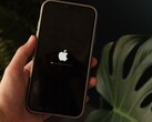 Hand hält ein iPhone, auf dem Display leuchtet das Apple-Logo mit Ladebalken.