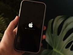 Hand hält ein iPhone, auf dem Display leuchtet das Apple-Logo mit Ladebalken.