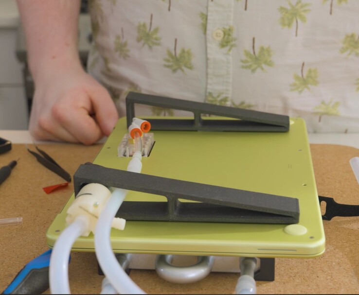 Modifiziertes MacBook Neo mit externer Pumpe und Schlauchsystem für DIY-Flüssigkeitskühlung.