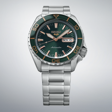 Seiko 5 Sports SKX HDB005 mit dunkelgrünem Zifferblatt, passender grüner Lünette, roségoldfarbenen Zeigern und Indizes sowie Edelstahlarmband vor hellgrauem Hintergrund