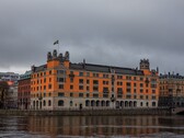 Orangefarbenes Rosenbad-Gebäude mit schwedischer Flagge am Wasser in Stockholm unter bewölktem Himmel
