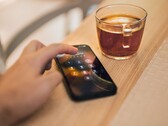 Hand tippt eine PIN auf einem Smartphone, das neben einem Glas Tee auf einem Holztisch liegt