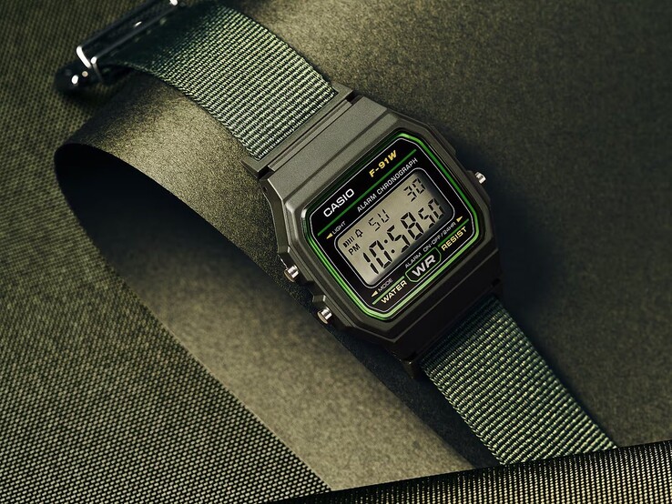 Casio F-91WF-3A Digitaluhr mit schwarzem Gehäuse, grünen Akzenten und gewebtem grünem Stoffarmband vor einem dunkelgrünen, strukturierten Hintergrund