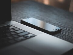 Smartphone liegt neben einem aufgeklappten Laptop auf einem dunklen Schreibtisch