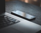 Smartphone liegt neben einem aufgeklappten Laptop auf einem dunklen Schreibtisch