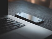 Smartphone liegt neben einem aufgeklappten Laptop auf einem dunklen Schreibtisch