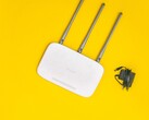 Weißer WLAN-Router mit drei Antennen und Netzteil auf gelbem Hintergrund