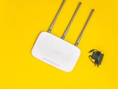 Weißer WLAN-Router mit drei Antennen und Netzteil auf gelbem Hintergrund