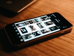 Smartphone liegt auf einem Holztisch und zeigt auf dem Display ein Raster aus Fotos