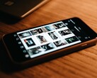 Smartphone liegt auf einem Holztisch und zeigt auf dem Display ein Raster aus Fotos