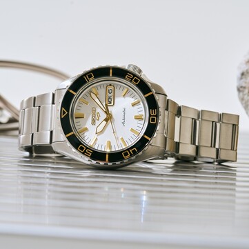 Seiko 5 Sports SKX HDB004 mit silberweißem Zifferblatt, schwarzer Drehlünette, goldfarbenen Zeigern und Indizes sowie Edelstahlarmband, schräg fotografiert