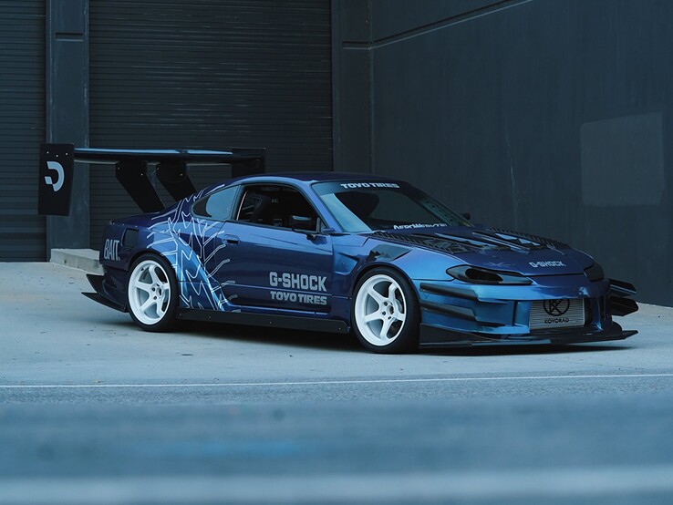 Ein blauer Driftwagen mit G-Shock- und Toyo-Tires-Branding ist vor einem Industriegebäude geparkt