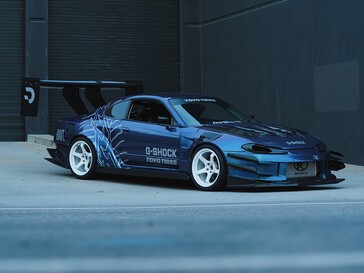 Ein blauer Driftwagen mit G‑Shock‑ und Toyo‑Tires‑Grafiken parkt vor einem Industriegebäude