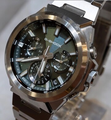 Nahaufnahme der Casio G-Shock GST-W1000D-3A mit grünem Zifferblatt, geometrischer Struktur, drei Hilfszifferblättern, Leuchtmarkierungen und polierter Edelstahl-Lünette