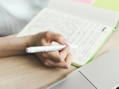 Person schreibt Notizen in ein Notizbuch neben einem aufgeklappten Laptop
