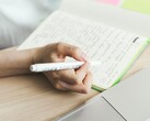 Person schreibt Notizen in ein Notizbuch neben einem aufgeklappten Laptop