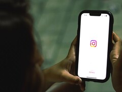 Frau hält ein Smartphone in beiden Händen, auf dem Display erscheint der Startbildschirm von Instagram