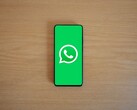 Smartphone auf einem Holztisch zeigt den grünen WhatsApp-Startbildschirm mit Logo.
