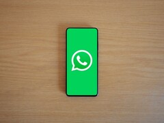 Smartphone auf einem Holztisch zeigt den grünen WhatsApp-Startbildschirm mit Logo.