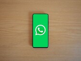 Smartphone auf einem Holztisch zeigt den grünen WhatsApp-Startbildschirm mit Logo.